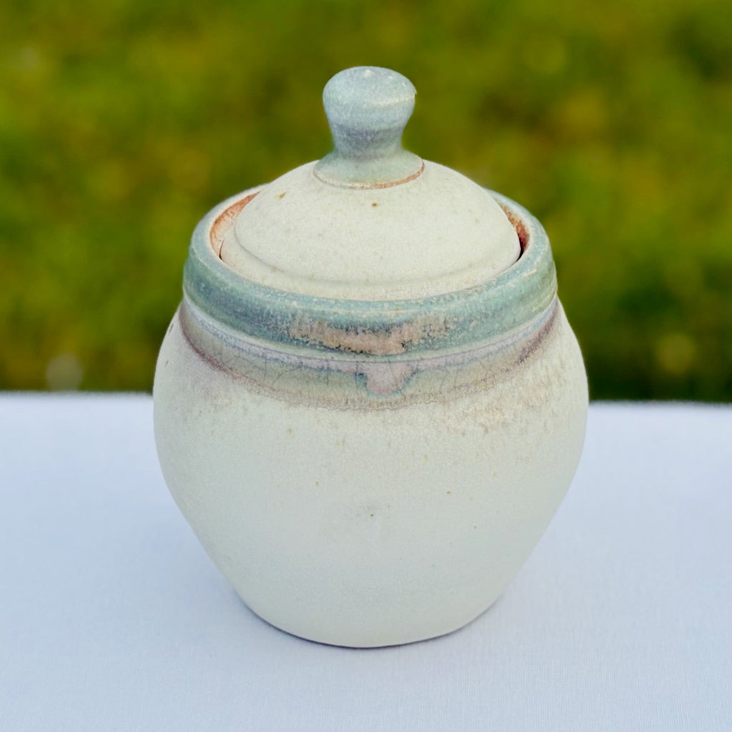 Delicate pottery jar with a matte green rim and soft white exterior with delicate lid with a light green knob made in Danbury, NC