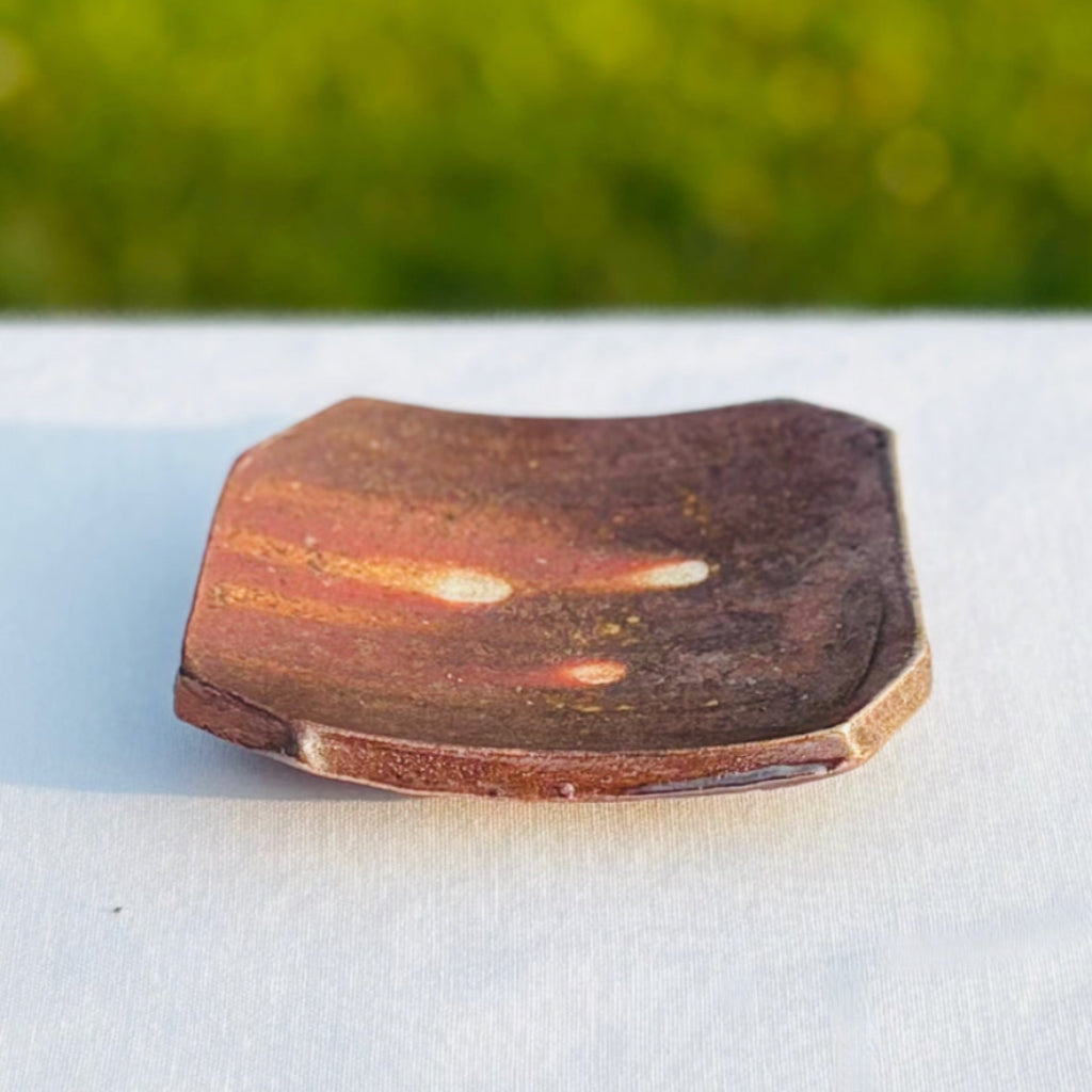 Wood-fired ceramic square soap dish with natural ash glaze showing orange flame patterns and earth tones with three white dots in the center and a subtle lines