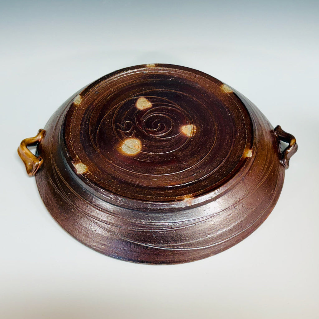 Bottom view: Handcrafted ceramic serving platter with blue spiral design on mahogany brown background and integrated handles, spirals and dots on the bottom.