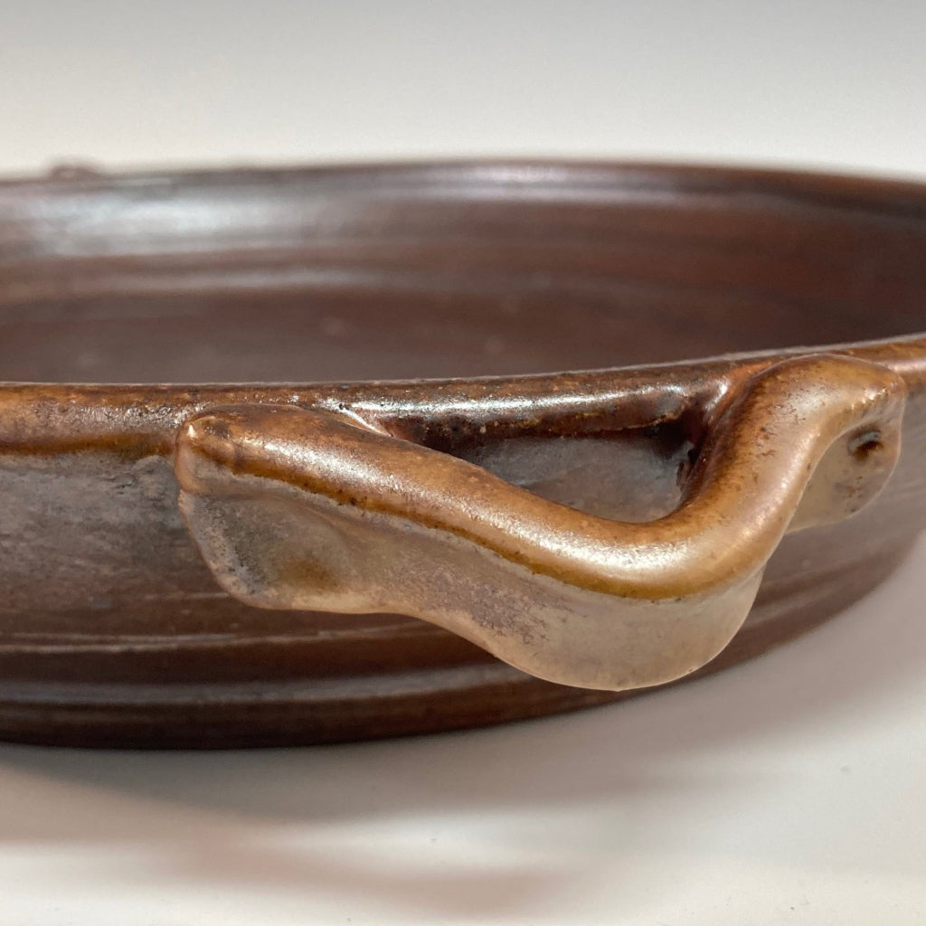 Up close image of handle: Handcrafted ceramic serving platter with spiral design on mahogany brown background and integrated handles.
