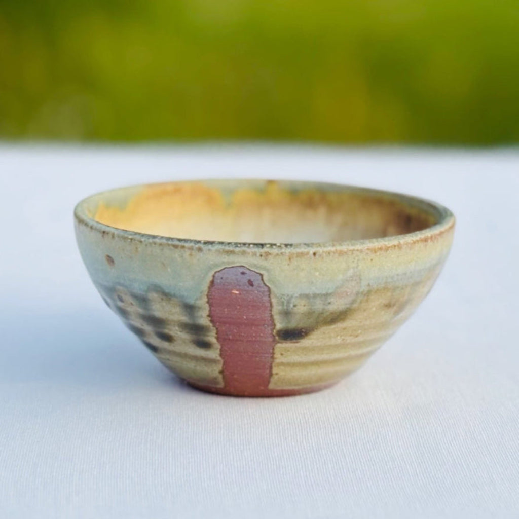 Handcrafted round ceramic ring dish with soft yellows and greens contrasting with rich amber brown stripe