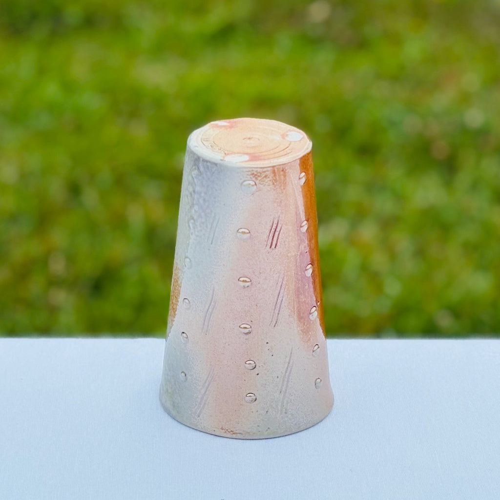 Artistic porcelain tumbler featuring unglazed bottom with swirl, artist mark, and three white wadding marks where cup made contact with a shelf during wood-firing