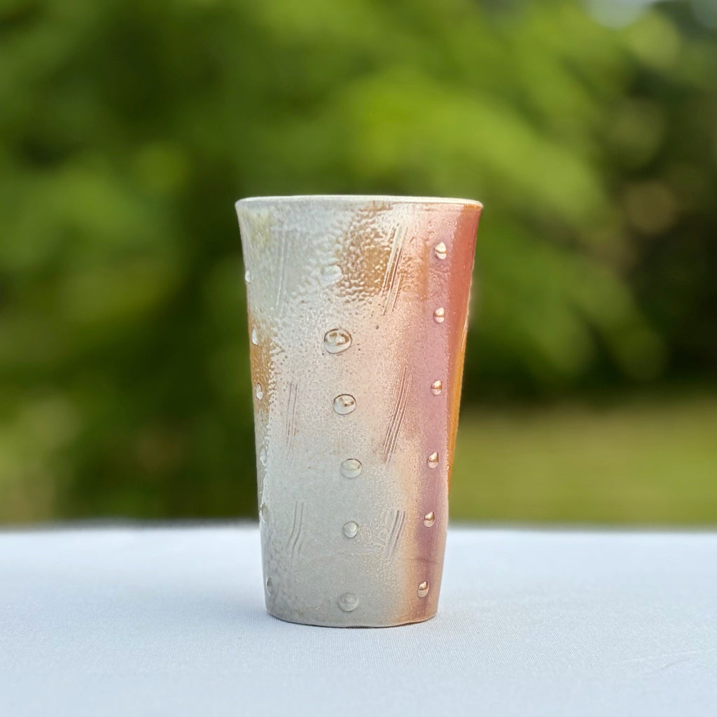 Lightweight porcelain tumbler featuring dots and incised lines and coppery metallic orange and glassy grey coloration 