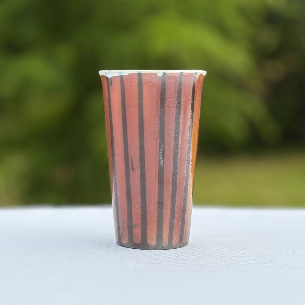 Porcelain cup with bold vertical black stripes that contrast with the soft peach and orange color of the unglazed cup