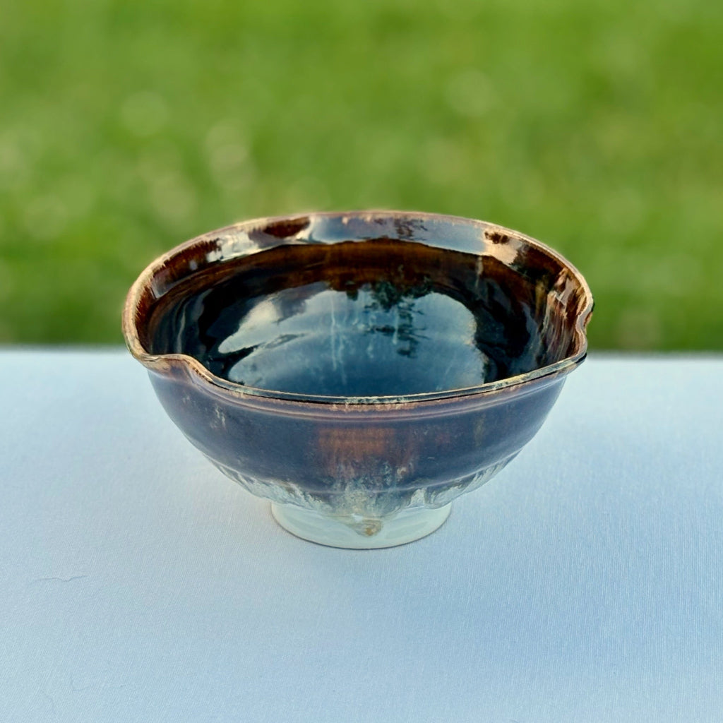 Dark glazed pottery bowl with smooth brown surface and lobed rim