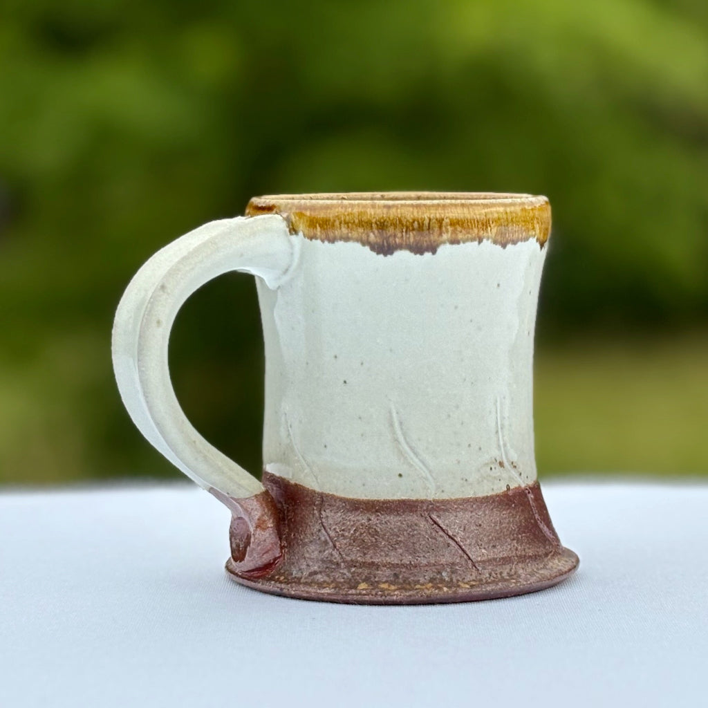 Pottery coffee mug with a gold rim which contrasts nicely with the glossy white glaze, and rich brown base. Delicate abstract carved decorations.