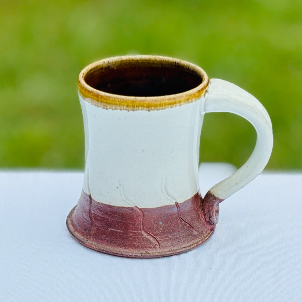Pottery mug with a deep brown interior, a gold rim which contrasts nicely with the glossy white glaze, and rich brown base. Delicate abstract carved decorations. 
