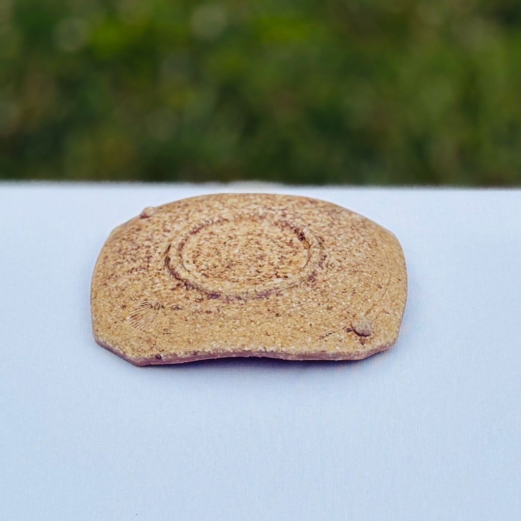 Wood-fired pottery soap dish displaying maker's mark, a raised circle, two delicate round feet, and a variegated pattern