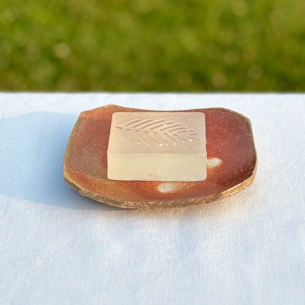 Handcrafted rectangular soap dish showing wood-fired color variations and ash deposit patterns with a bar of soap with a leaf pattern